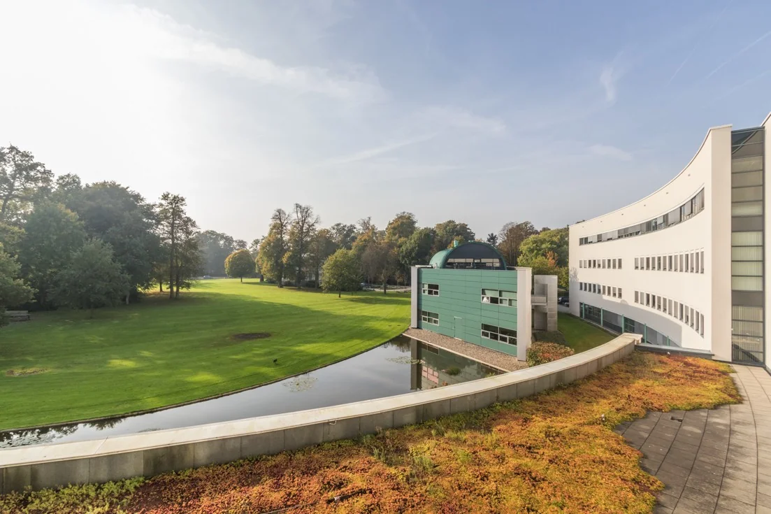 Modern kantoorgebouw Sparrenheuvel met gebogen architectuur, gelegen aan een groen grasveld en omgeven door bomen.