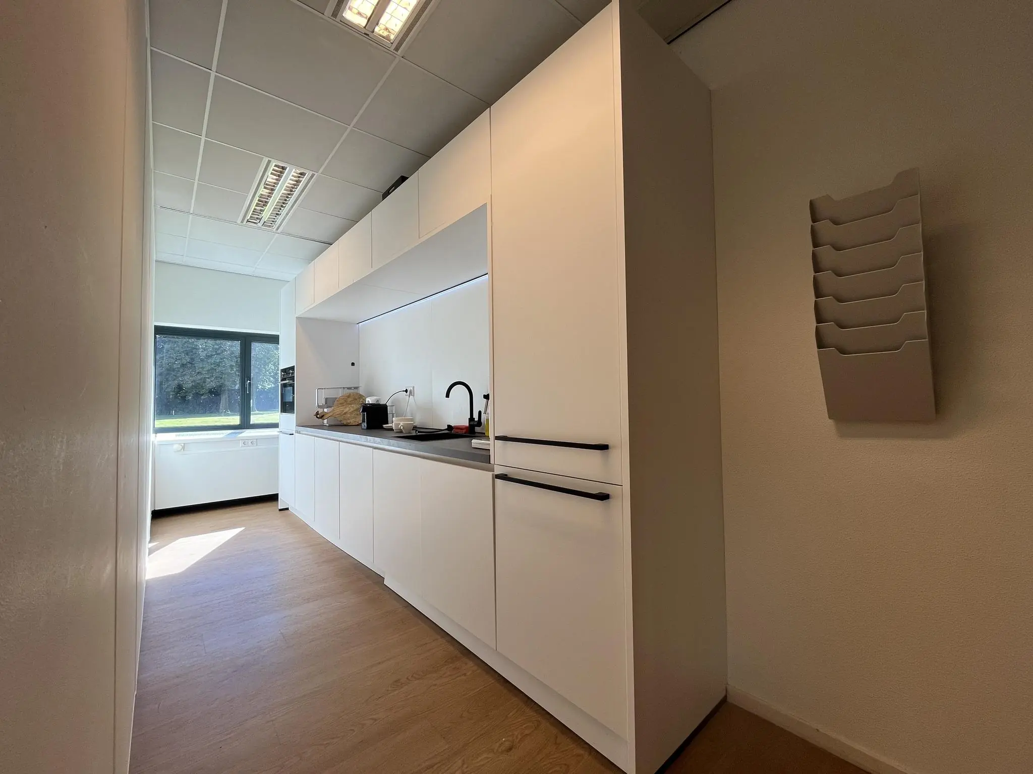 Moderne kitchenette met witte kasten en zwart kraanwerk in kantoorruimte Sparrenheuvel.
