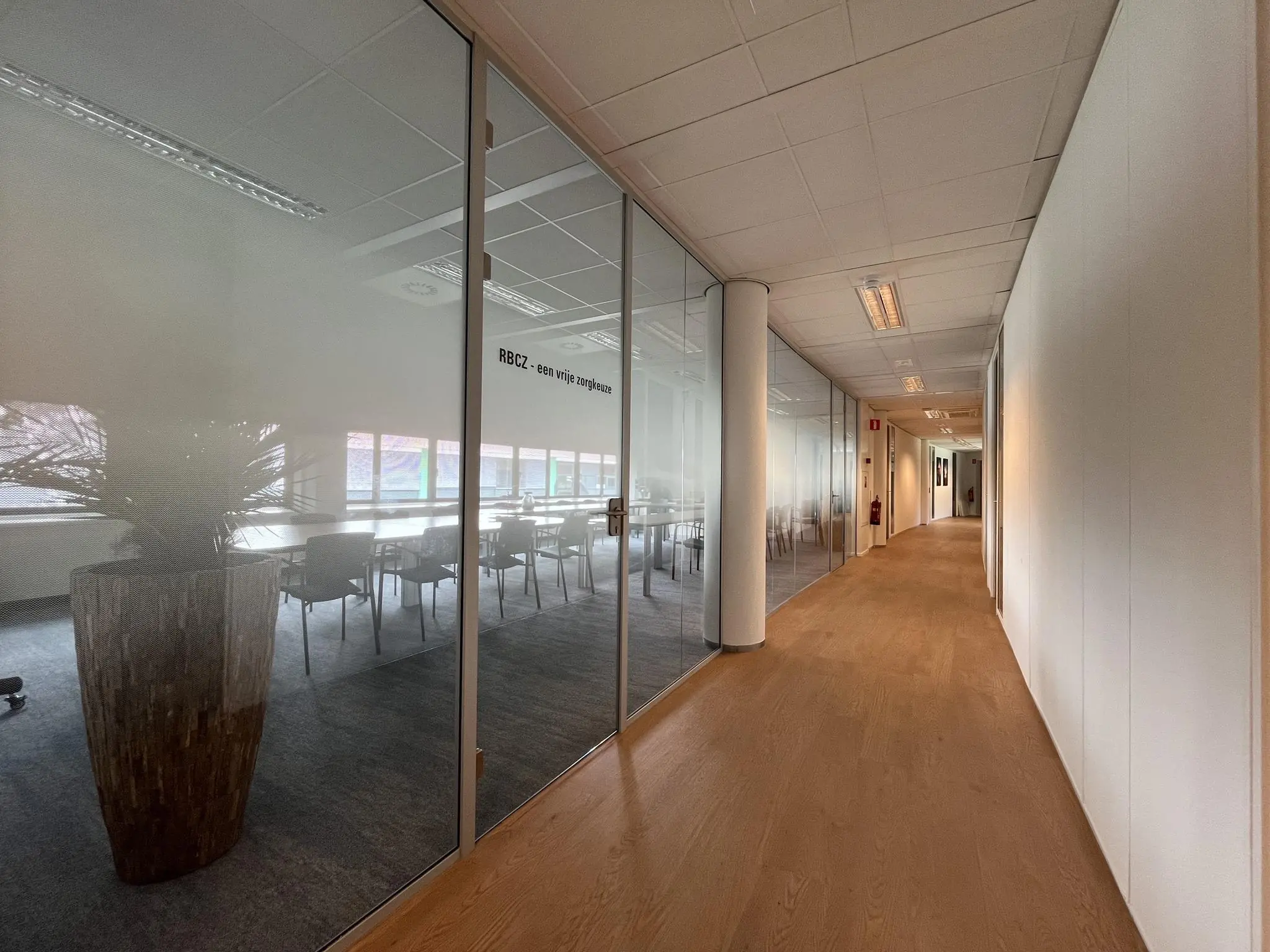 Lichte kantoorruimte met een glazen vergaderruimte aan de linkerzijde in het gebouw Sparrenheuvel.