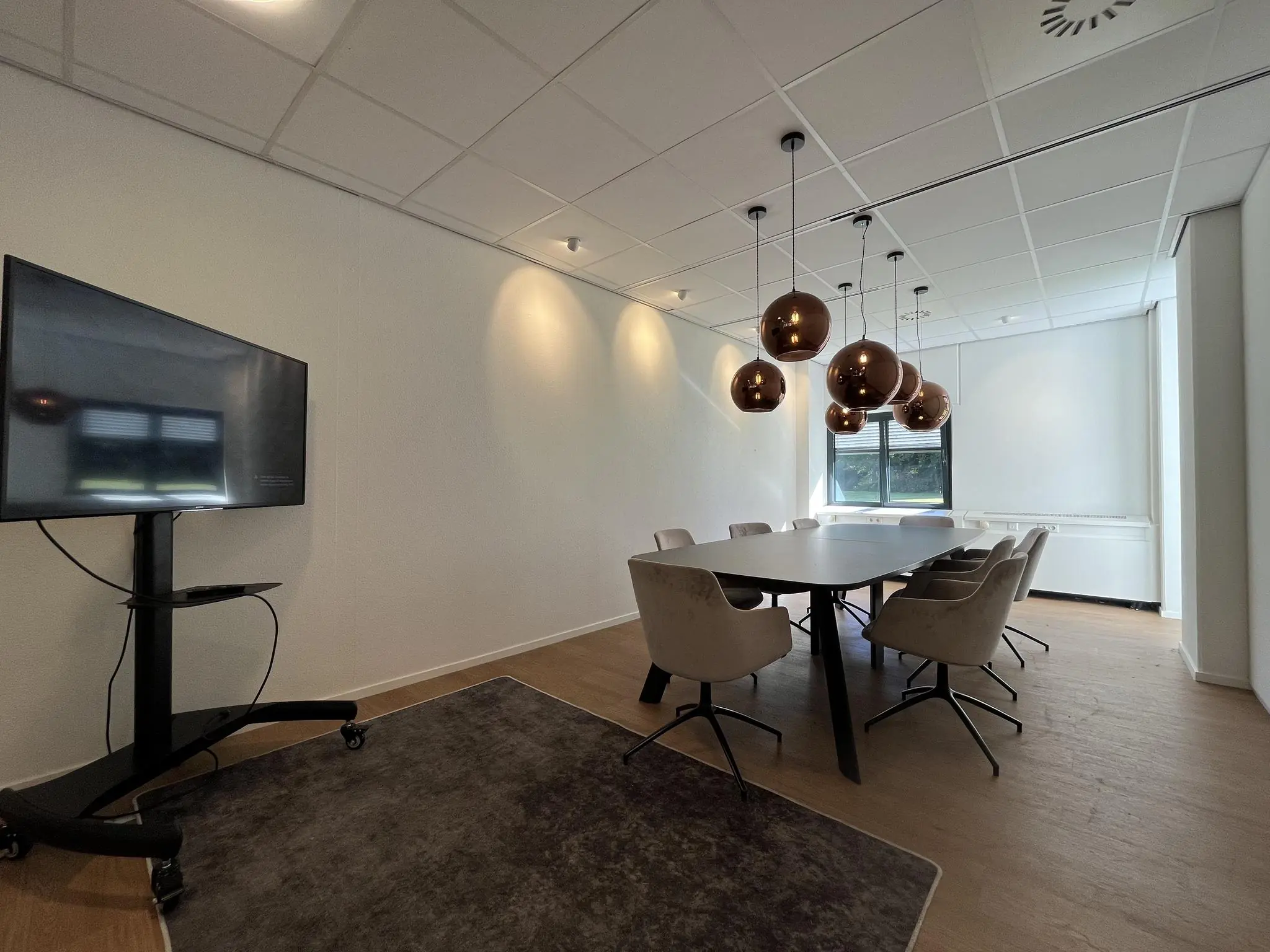 Vergaderruimte Sparrenheuvel met een lange tafel, moderne stoelen, hanglampen en een presentatiescherm.