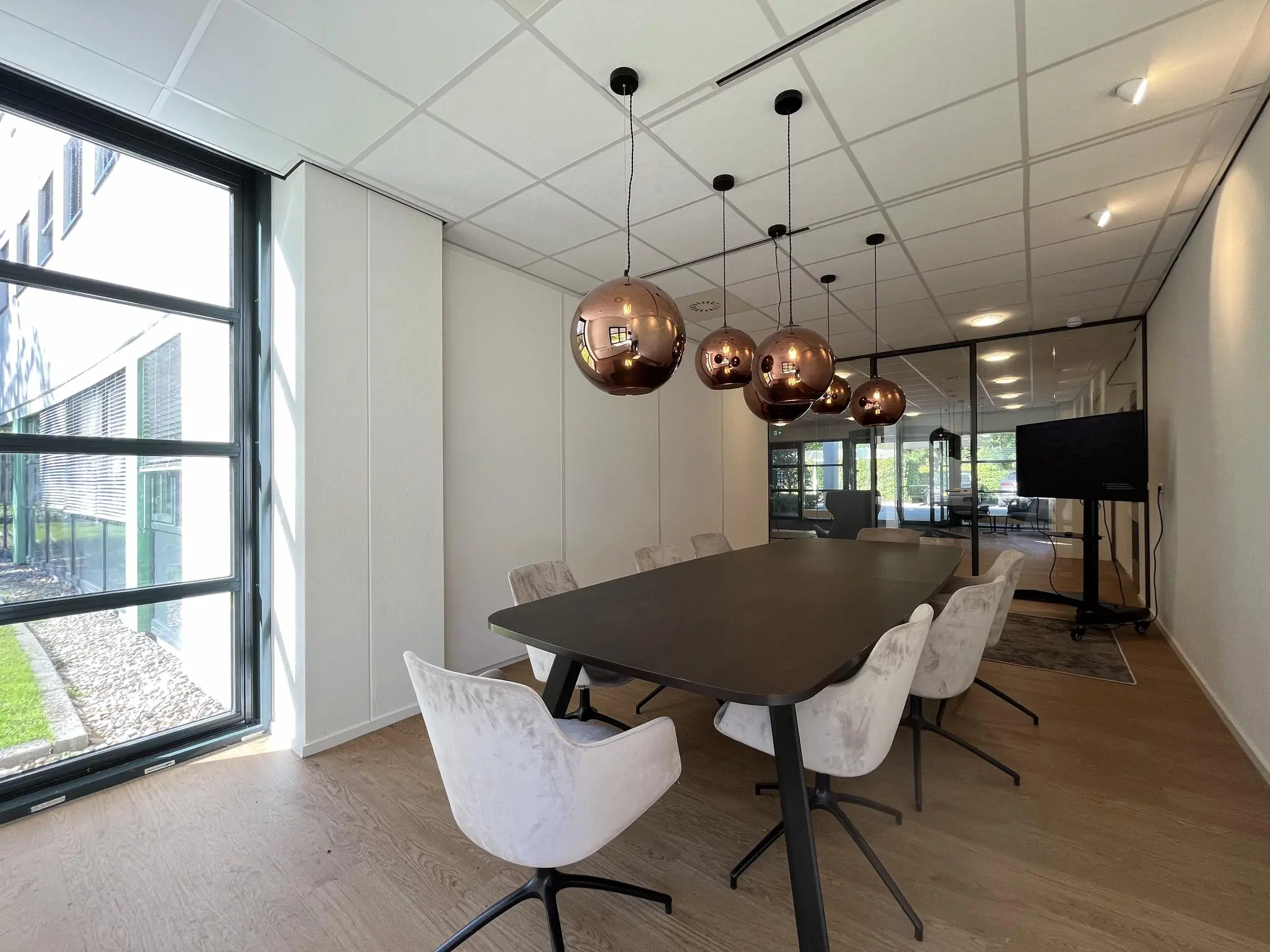 Vergaderruimte op Sparrenheuvel met moderne inrichting, grote raampartij en koperkleurige hanglampen.