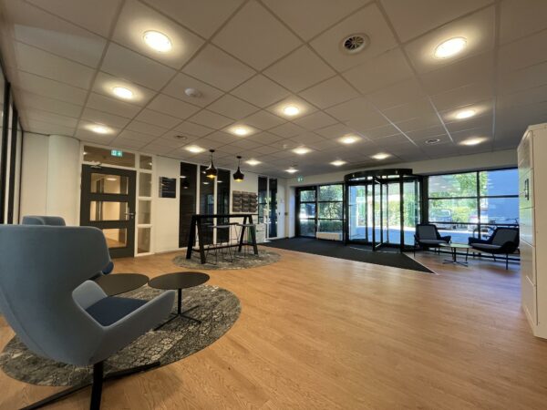 Moderne en ruimtelijke entreehal van gebouw Sparrenheuvel met zitplaatsen en een draaideur.