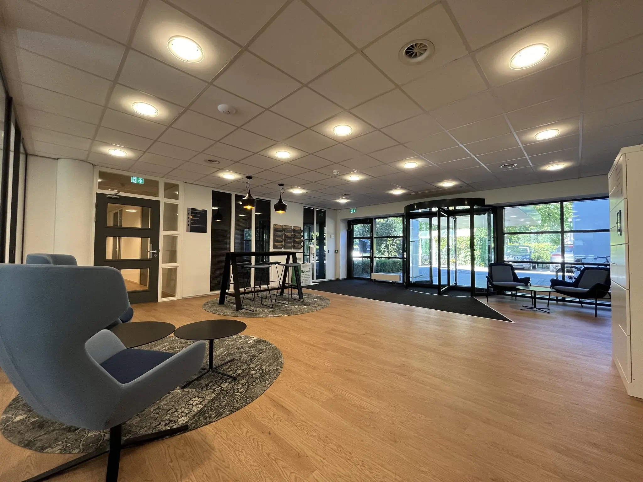 Moderne en ruimtelijke entreehal van gebouw Sparrenheuvel met zitplaatsen en een draaideur.