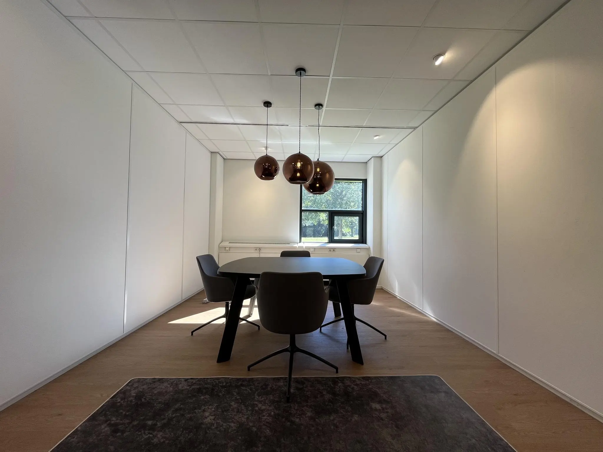 Vergaderruimte op Sparrenheuvel met een ovalen tafel, vier stoelen en drie hanglampen bij een raam.