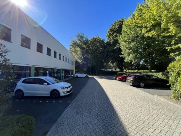 Parkeergelegenheid bij kantoorpand Sparrenheuvel met geparkeerde auto's en omliggende bomen in de zon.