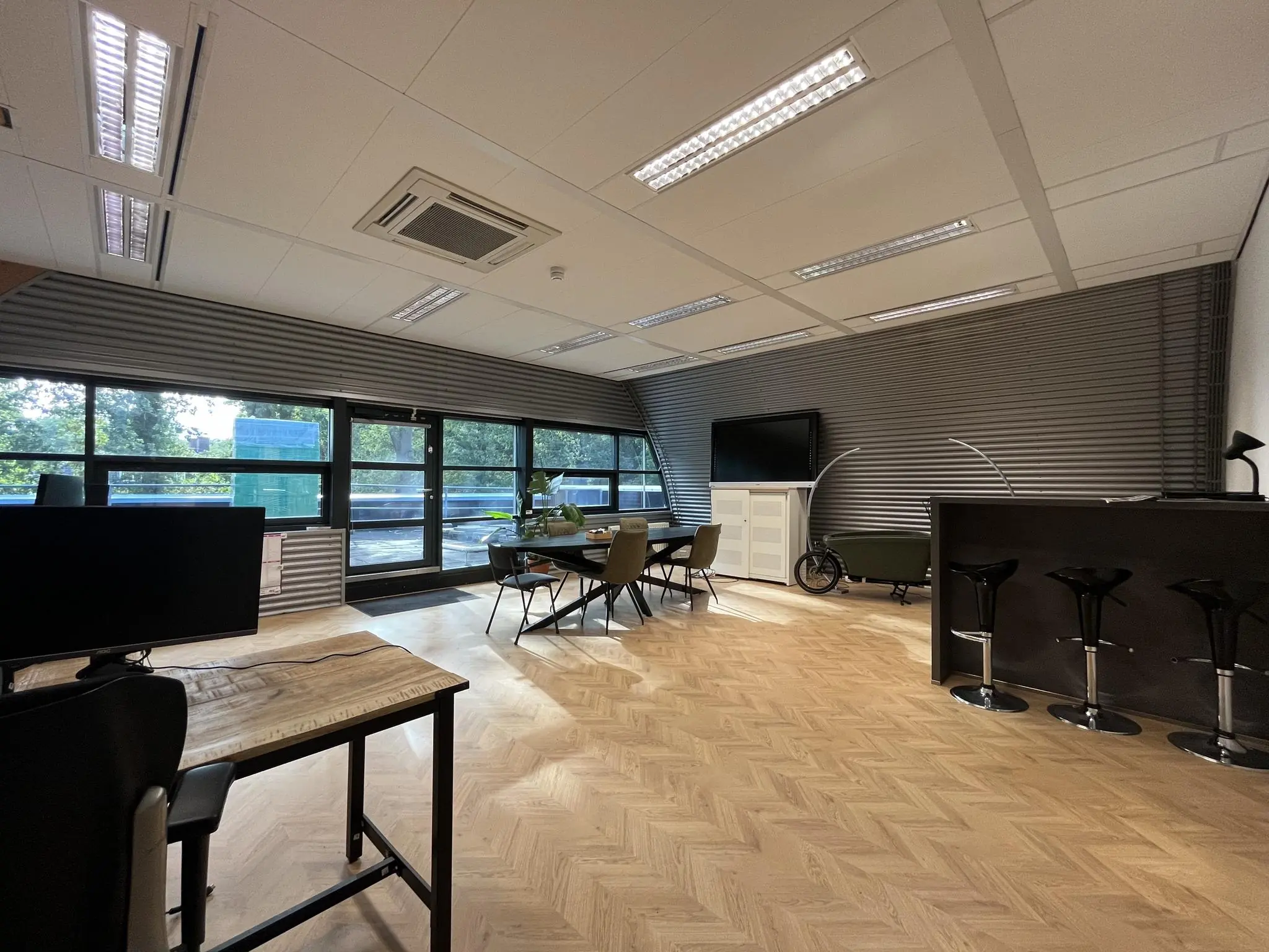 Moderne kantoorruimte op Sparrenheuvel met houten visgraatvloer, grote ramen en een vergadertafel.