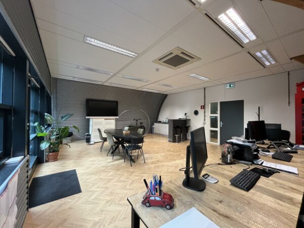 Moderne kantoorruimte op Sparrenheuvel met werkplekken, vergadertafel, planten en grote televisie aan de wand.