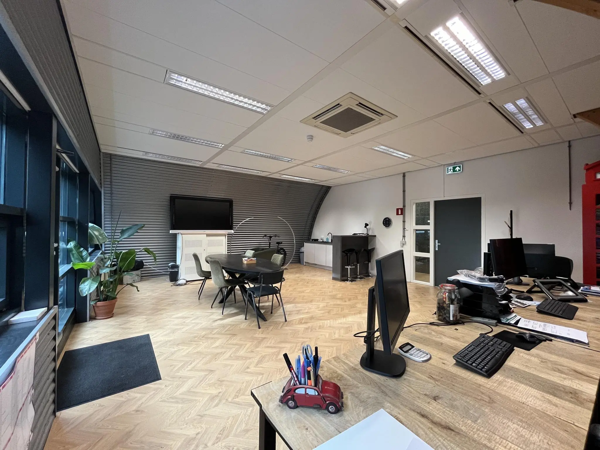Moderne kantoorruimte op Sparrenheuvel met werkplekken, vergadertafel, planten en grote televisie aan de wand.