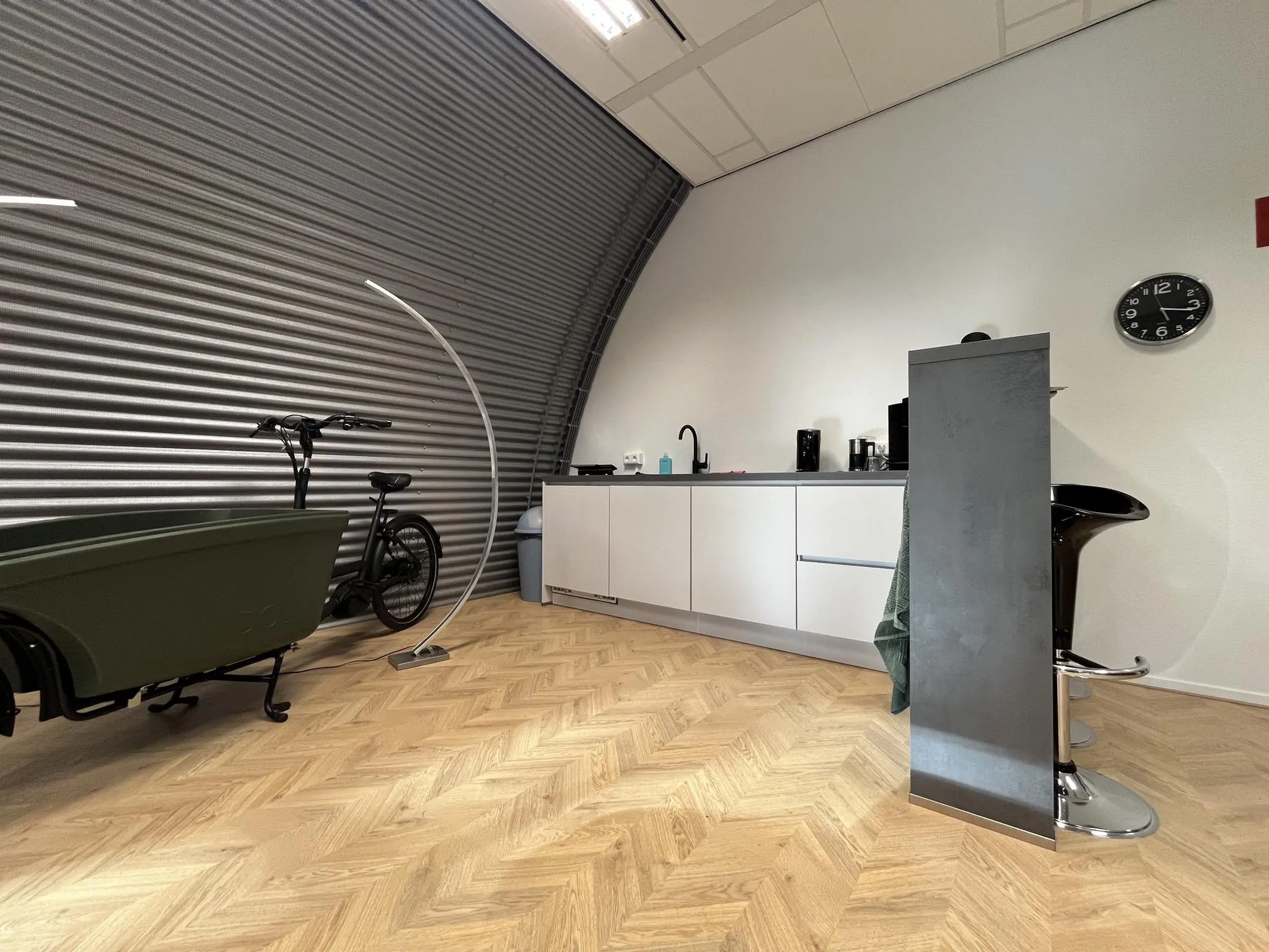Moderne pantryruimte in kantoor Sparrenheuvel met houten visgraatvloer, designkeuken en bakfiets tegen een metalen wand.
