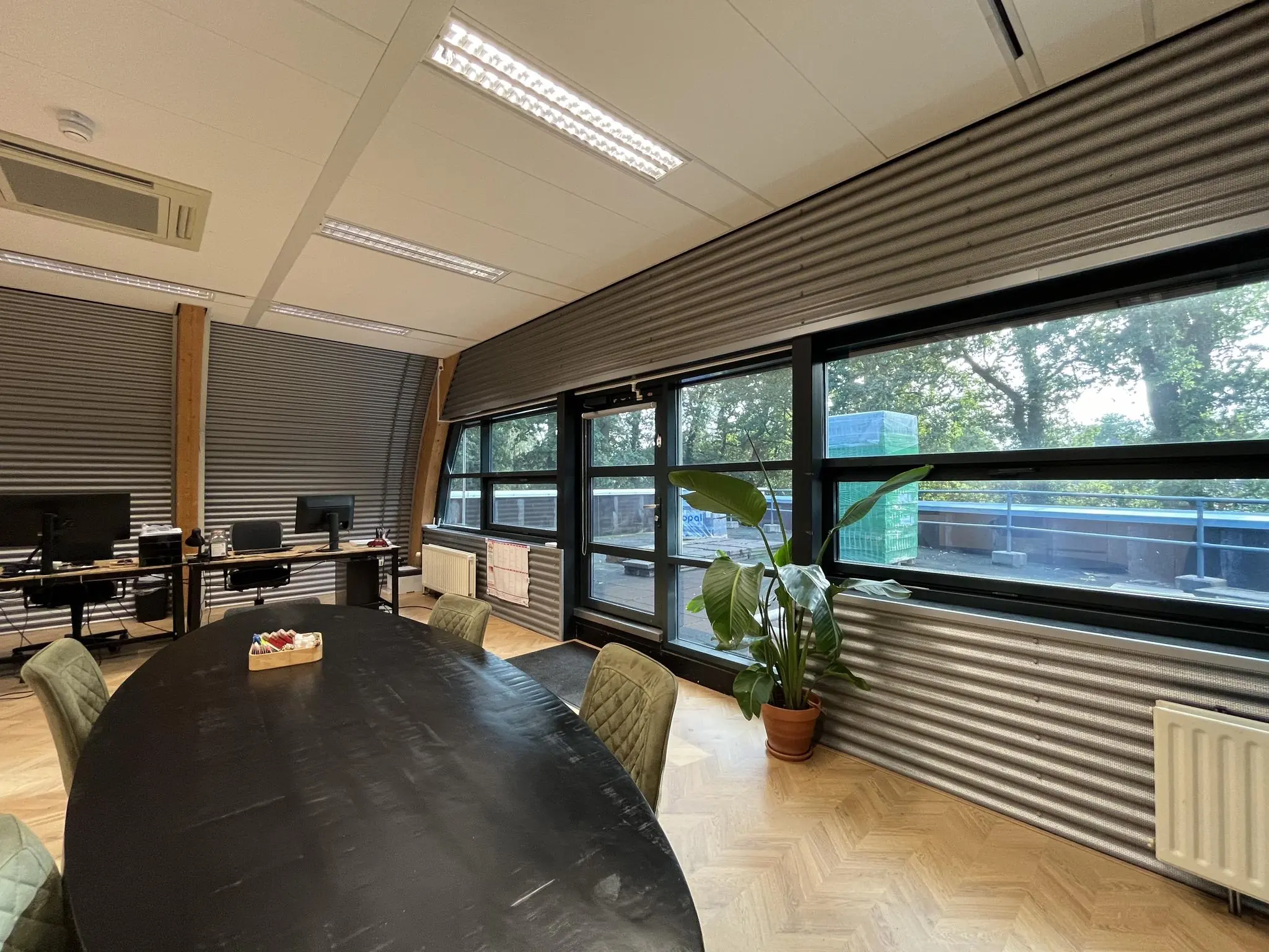 Moderne kantoorruimte met een ovale vergadertafel, werkplekken, grote ramen en uitzicht op een groene buitenomgeving bij Sparrenheuvel.