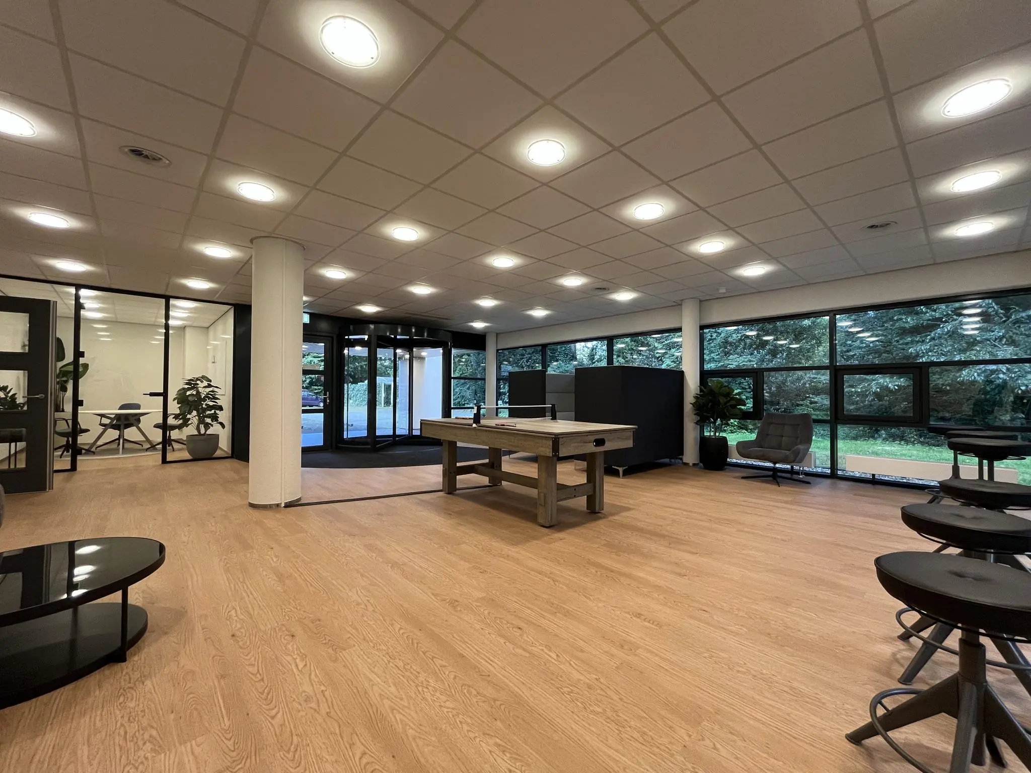 Moderne, ruime kantoorlobby van Sparrenheuvel met houten vloer, een tafeltennistafel en grote ramen met uitzicht op groen.