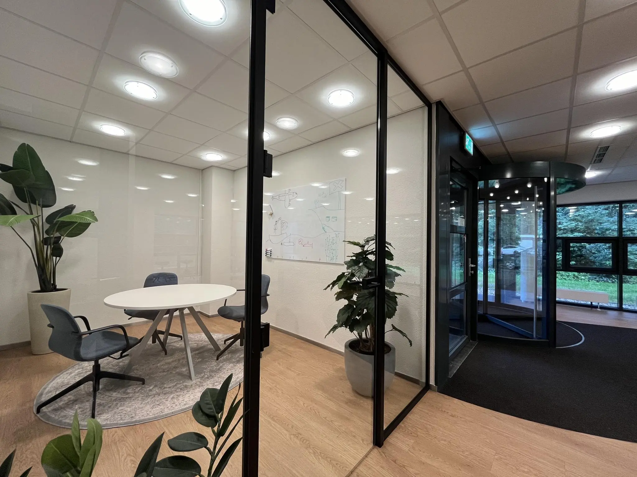 Moderne vergaderruimte bij kantoor Sparrenheuvel met glazen wanden, ronde tafel en draaideur bij de ingang.