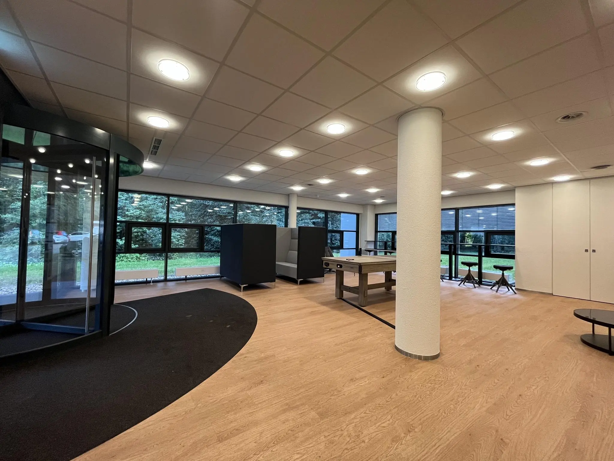 Modern ingerichte ontvangstruimte van Sparrenheuvel met zitplaatsen, een pooltafel en grote ramen met uitzicht op groen.