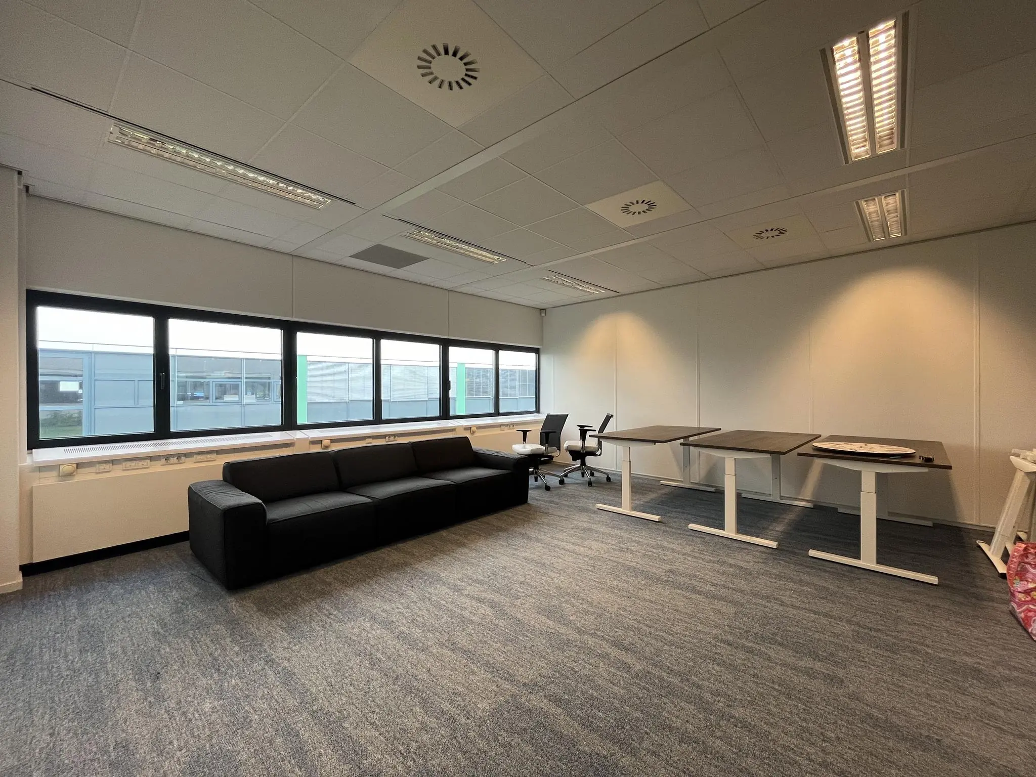 Moderne, ruime kantoorruimte in gebouw Sparrenheuvel met bureaus, stoelen en een zwarte bank langs het raam.