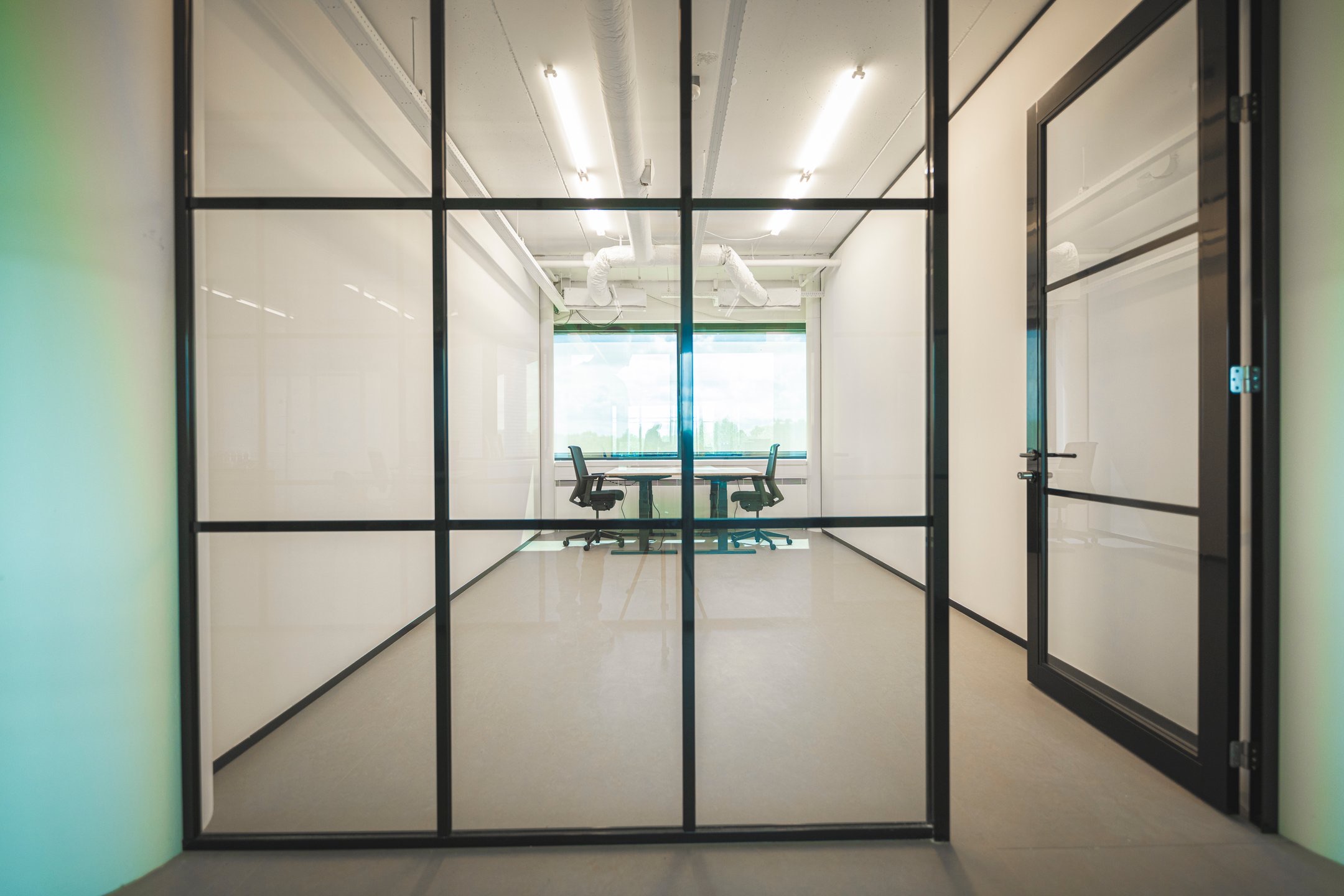 Vergaderruimte met glazen wanden, een houten tafel en bureaustoelen, gezien van buiten de kamer.