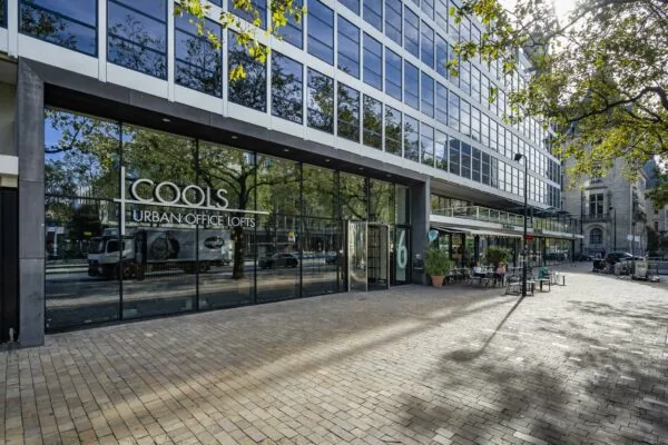 Glazen gevel van COOLS Urban Office Lofts aan de Coolsingel in Rotterdam met zitgelegenheid op het plein ervoor.