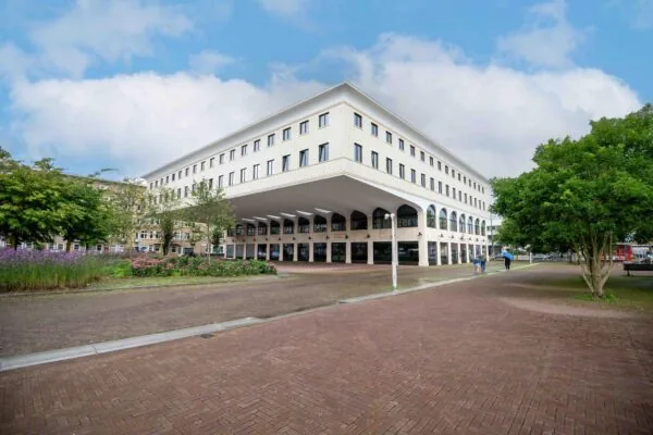 Modern wit gebouw met boogconstructie op het Stadionplein in Amsterdam, omgeven door groen en bestrating.