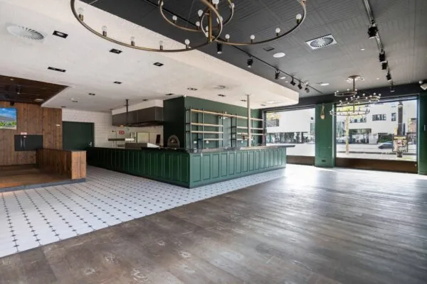 Interieur van een leeg restaurant aan het Stadionplein met een groene bar, open keuken en grote ramen aan de straatzijde.