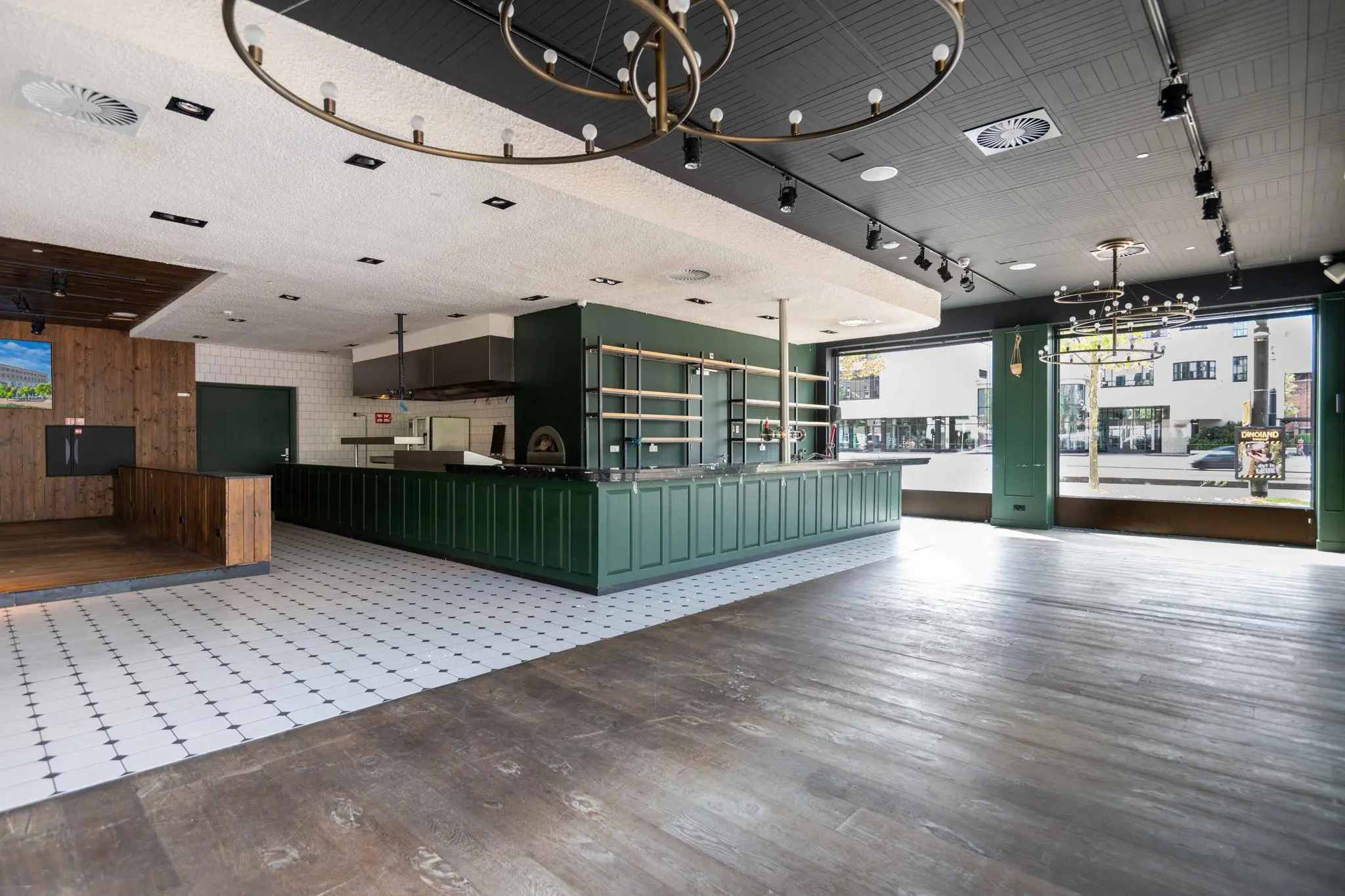Interieur van een leeg restaurant aan het Stadionplein met een groene bar, open keuken en grote ramen aan de straatzijde.