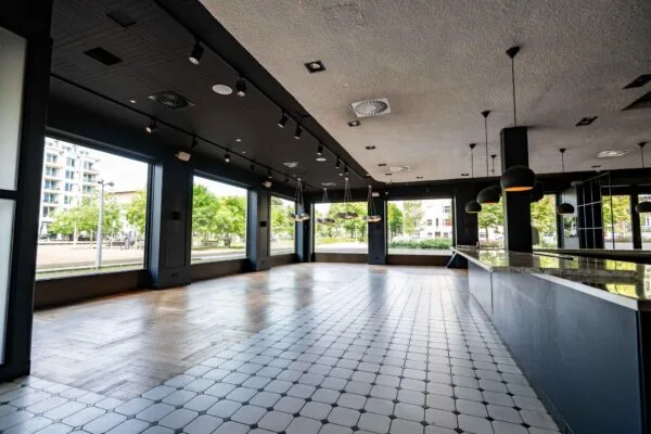 Leeg horecapand met grote ramen aan het Stadionplein in Amsterdam, met een zwart plafond en tegelvloer.