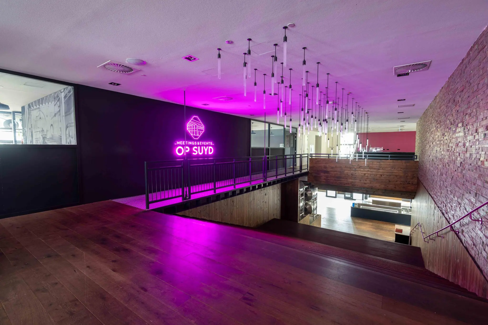 Interieur van evenementenlocatie Op Suyd met trap, houten vloeren en opvallende paarse neonverlichting.