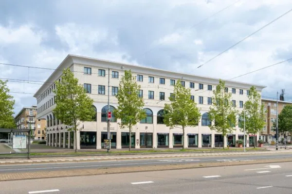 Modern hoekgebouw aan het Stadionplein in Amsterdam met bomenrij en tramhalte op de voorgrond.