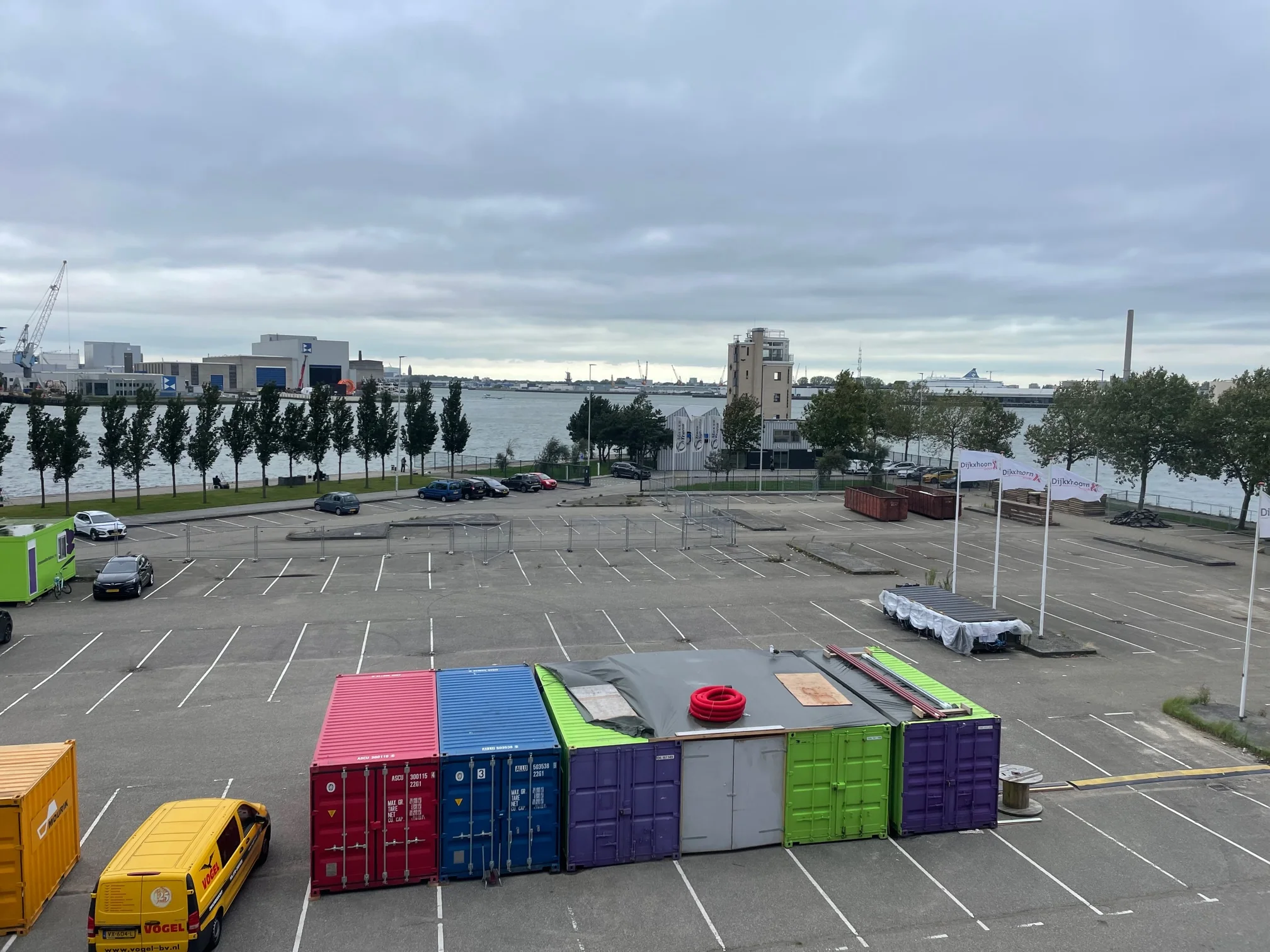 Leeg parkeerterrein aan de Sluisjesdijk met gekleurde containers, geparkeerde voertuigen en uitzicht op de haven.