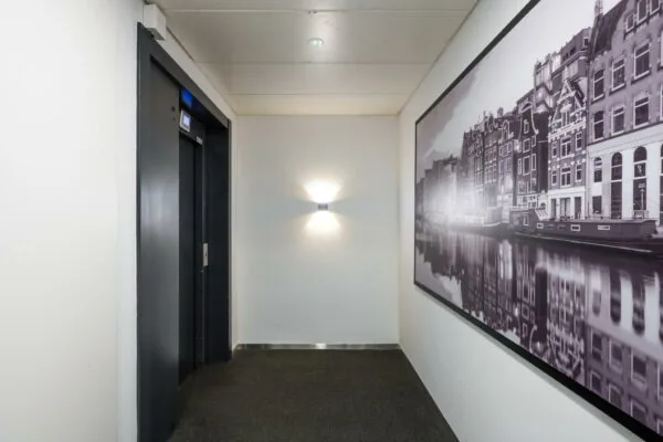 Hal met een liftdeur en een grote zwart-wit foto van Amsterdamse grachtenhuizen aan de muur.