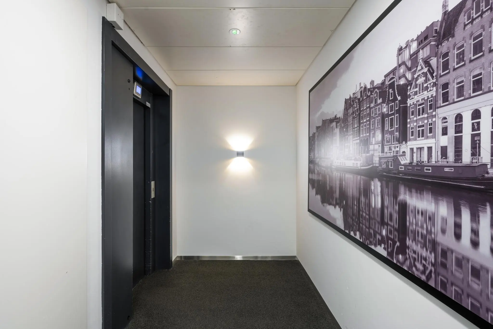 Hal met een liftdeur en een grote zwart-wit foto van Amsterdamse grachtenhuizen aan de muur.