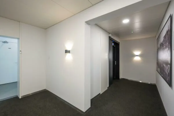 Hal met een liftdeur, een open toiletruimte en wandverlichting in het gebouw Backershagen.