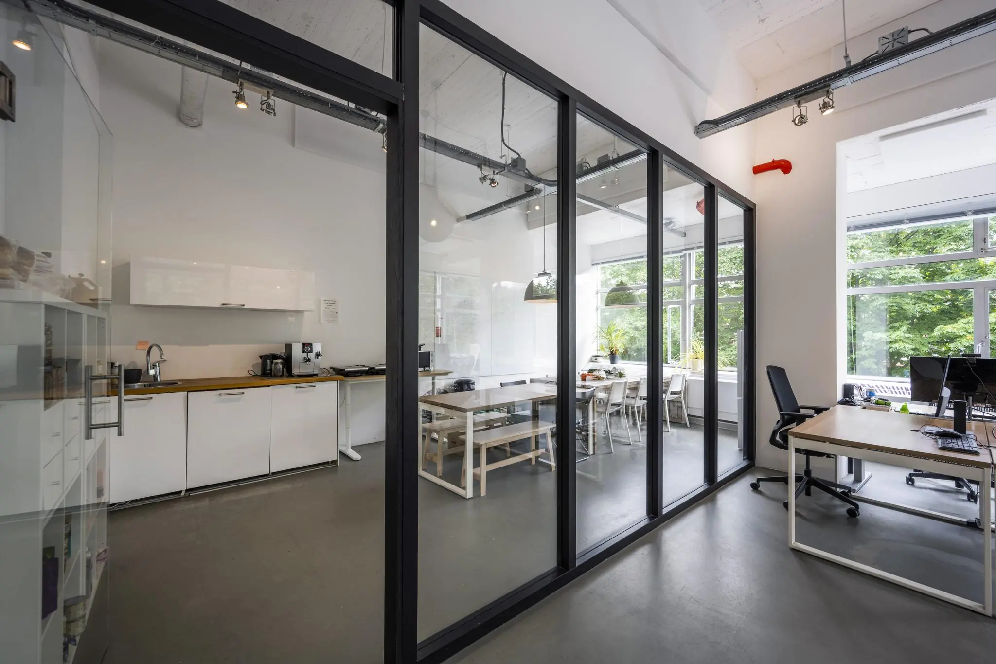Moderne kantoorruimte met glazen vergaderruimte, open keuken en werkplekken bij het raam.