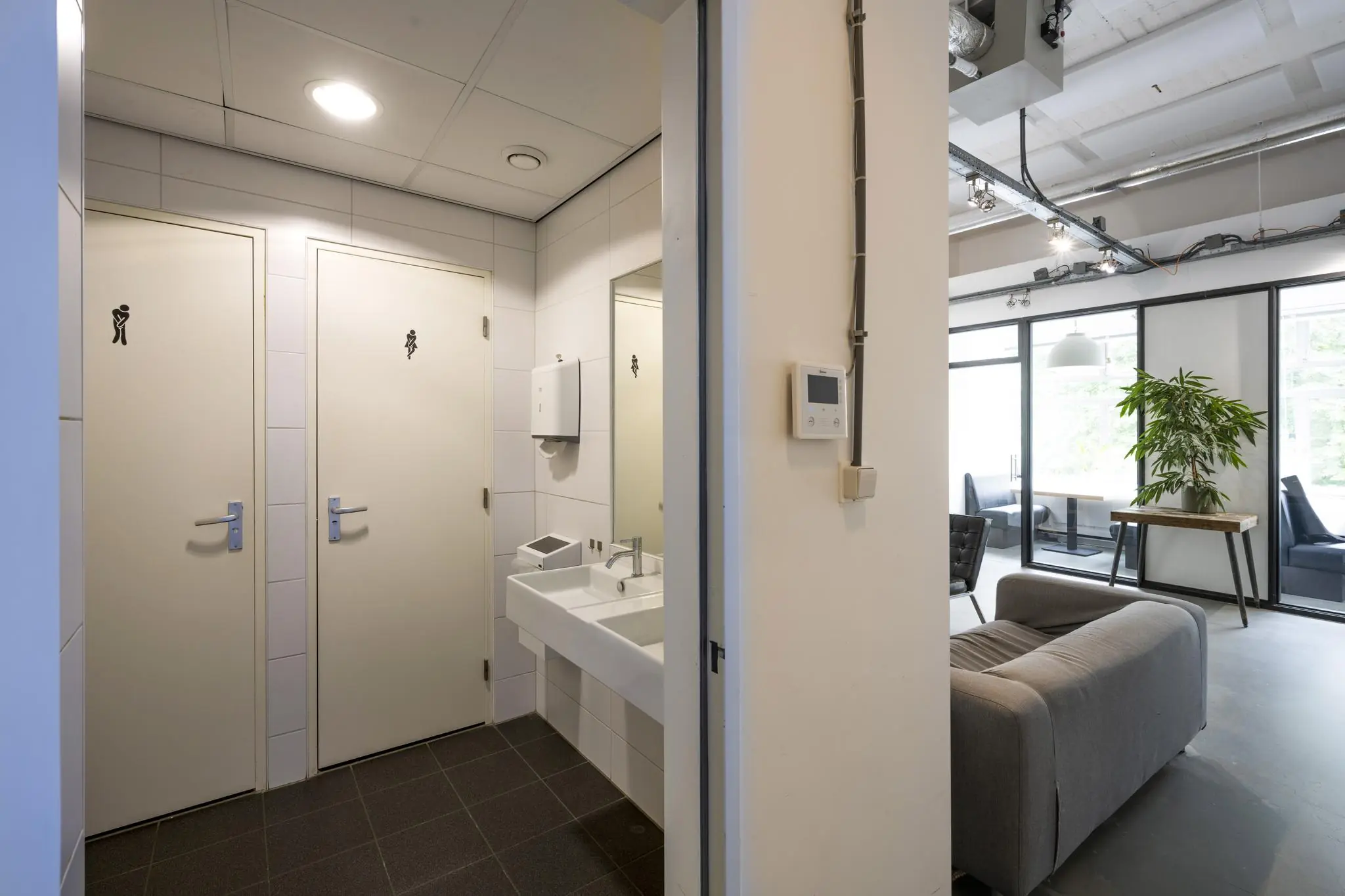 Hal met toiletruimte en wasbak, grenzend aan een moderne loungeruimte in kantoorpand Backershagen.
