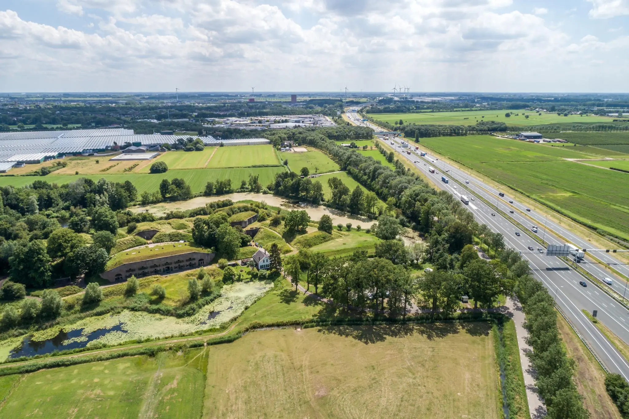 Luchtfoto van Fort bij Veldhuis aan de Fortweg, gelegen naast snelweg A9 en omringd door landerijen en kassen.