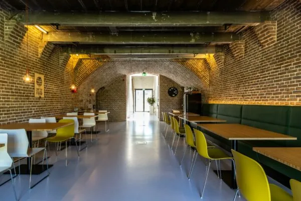 Moderne eetruimte met gele en witte stoelen in een gerestaureerde ruimte met bakstenen gewelven aan de Fortweg.