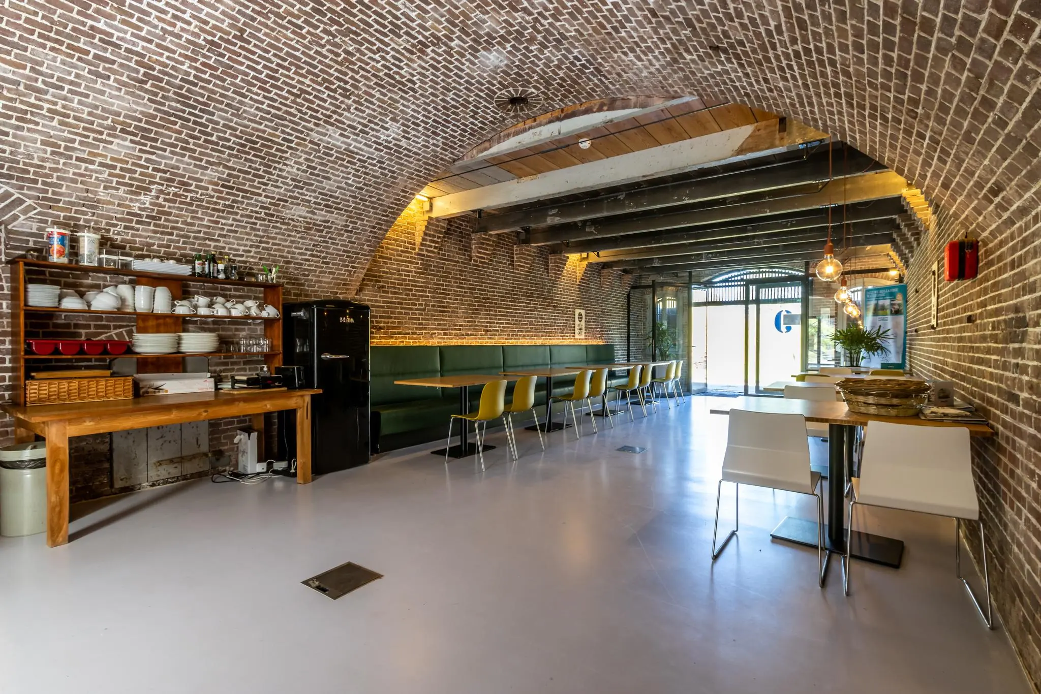 Modern ingerichte ruimte met bakstenen gewelfd plafond, lange eettafel met gele stoelen en open keukenblok aan de Fortweg.