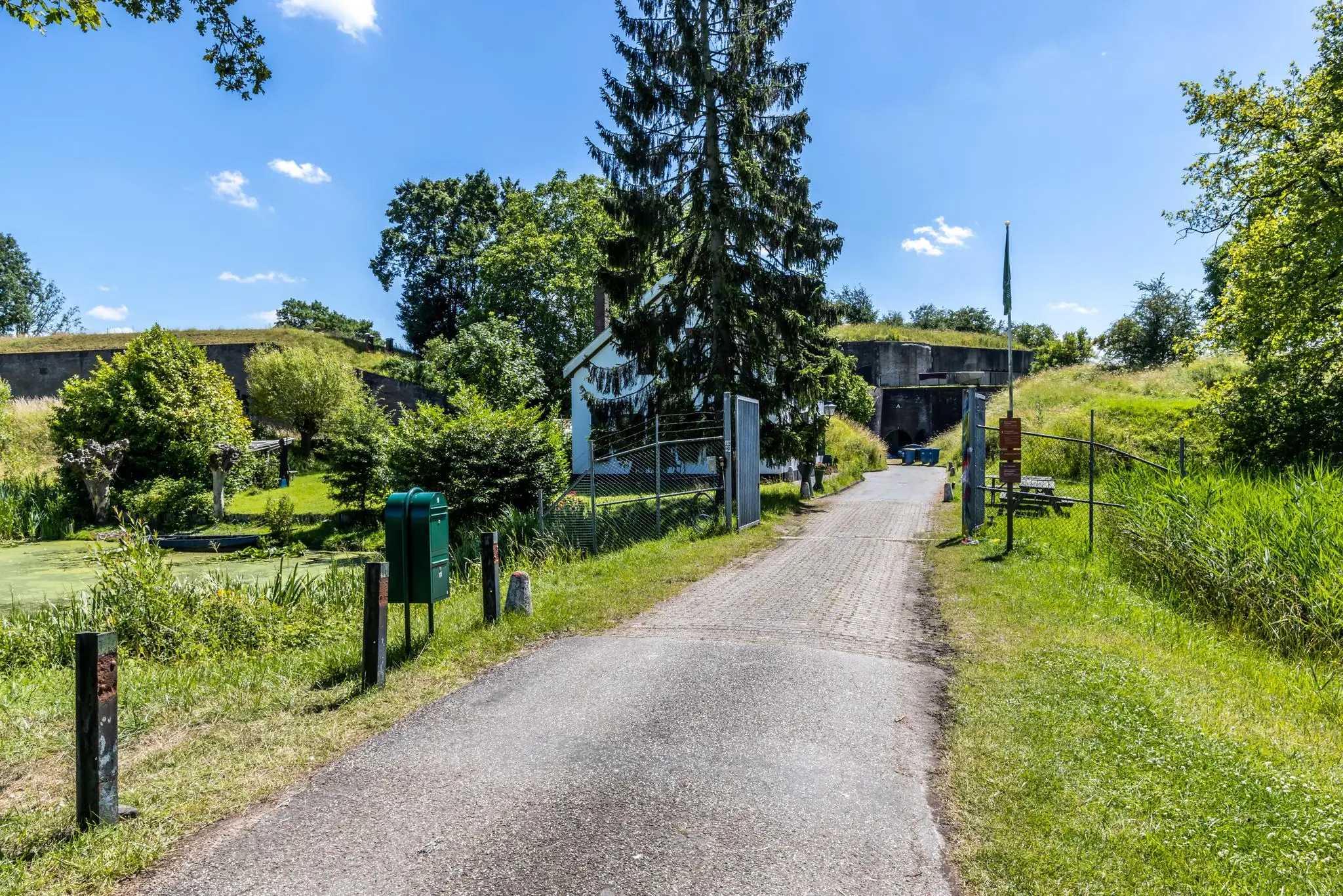 Ingang van Fort bij Rijnauwen aan de Fortweg, omringd door groen en een heldere blauwe lucht.