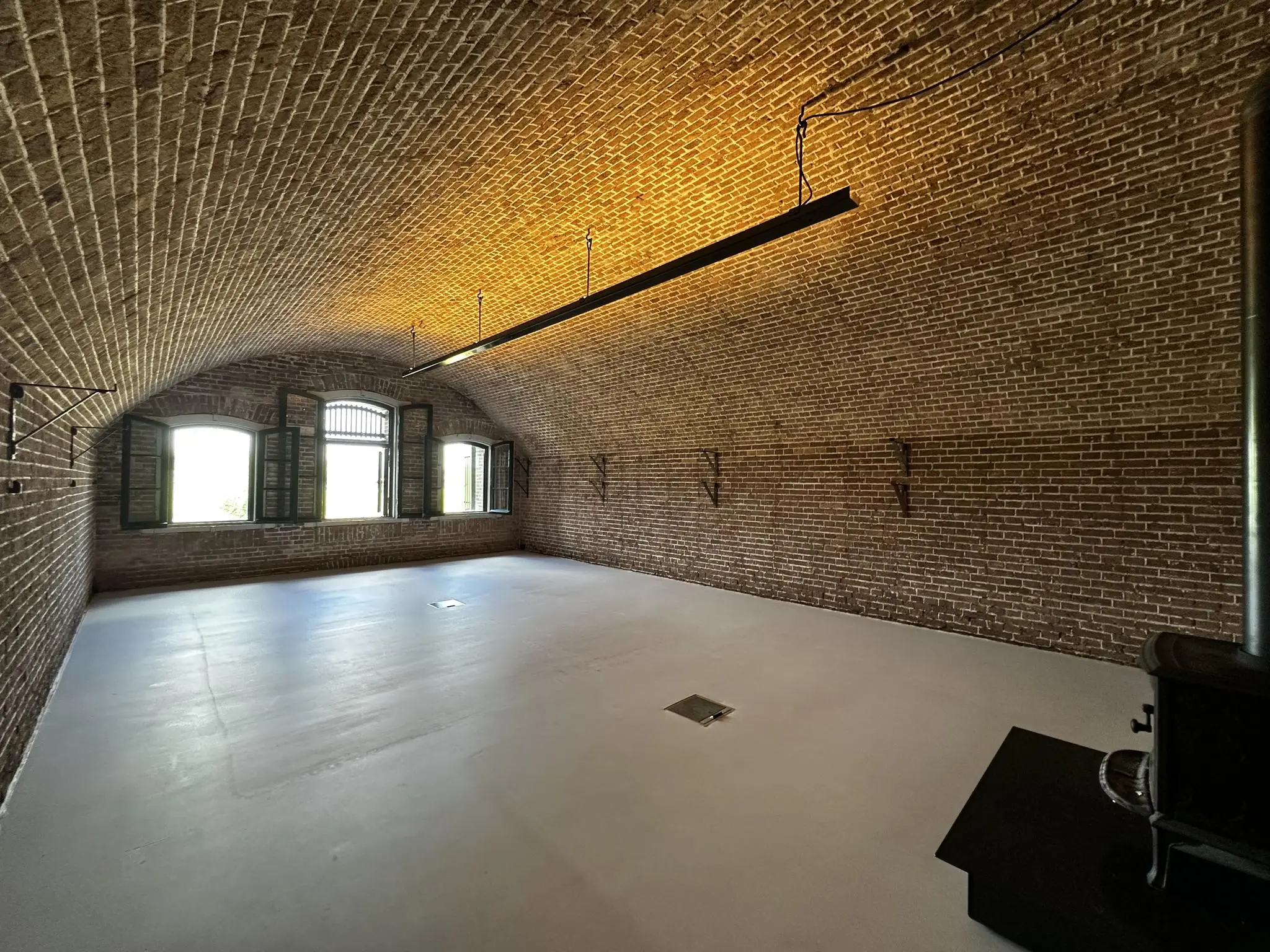 Ruime, bakstenen kamer in Fort bij de Fortweg met tongewelf, open ramen en een houtkachel.