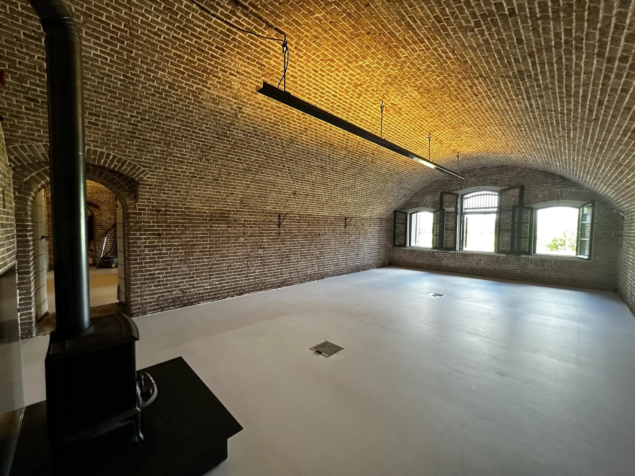 Ruime, gerenoveerde kamer in Fortweg met een gewelfd bakstenen plafond, houten kachel en openstaande ramen.