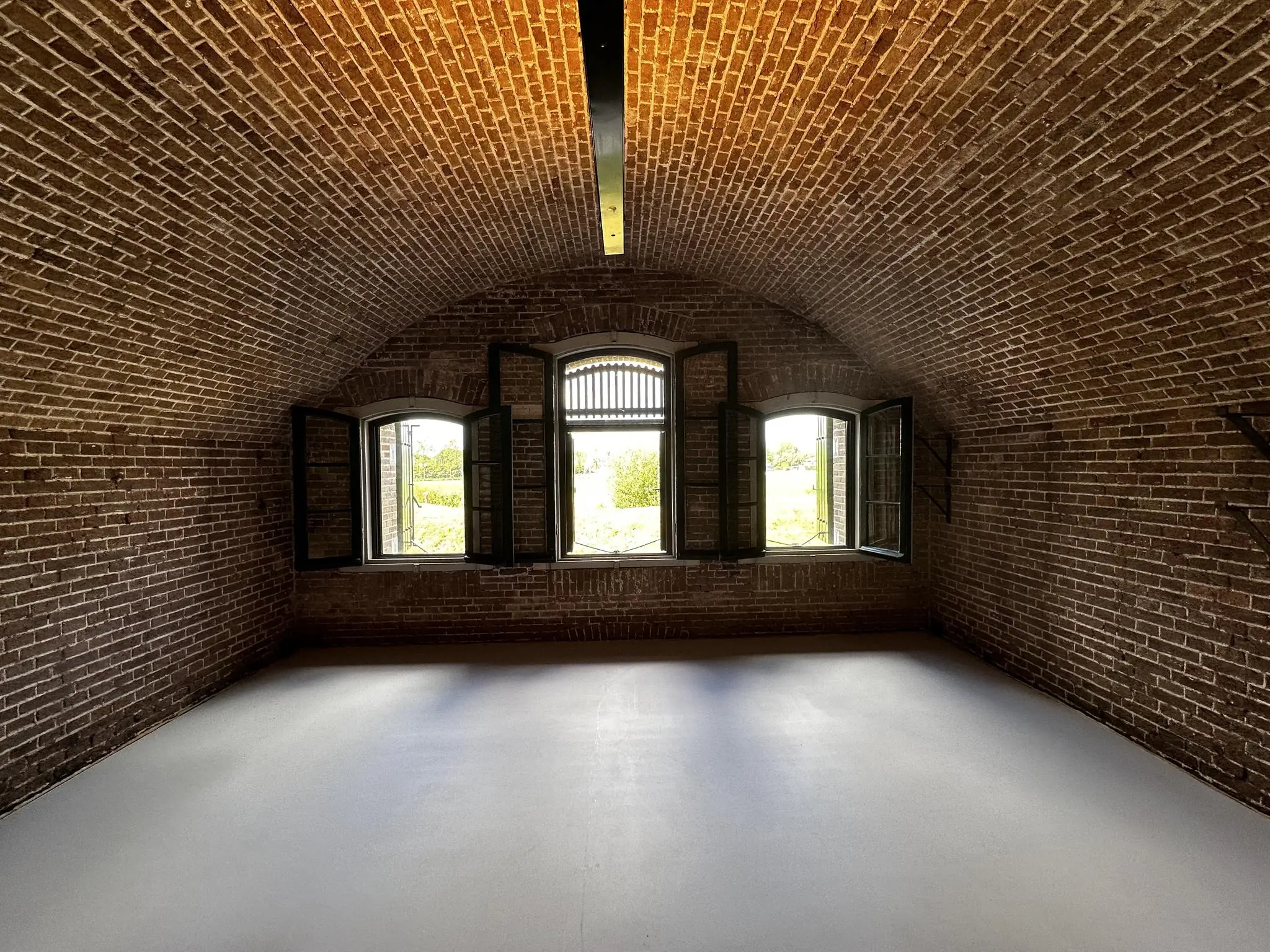 Binnenruimte met gewelfd plafond in Fort bij de Fortweg, met open ramen die uitkijken op het groene landschap.