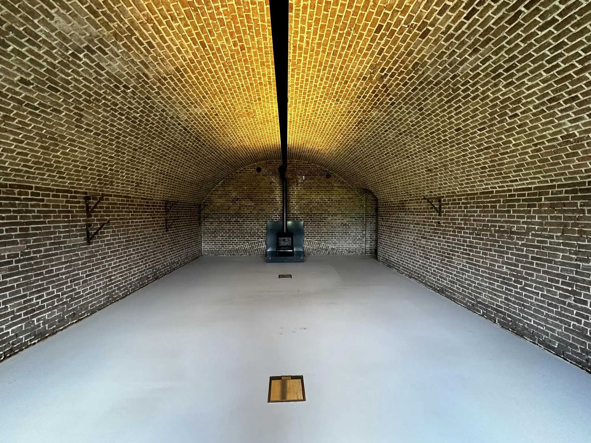 Interieur van een lege gemetselde fortgang met tongewelf en een zwarte kachel aan het einde.
