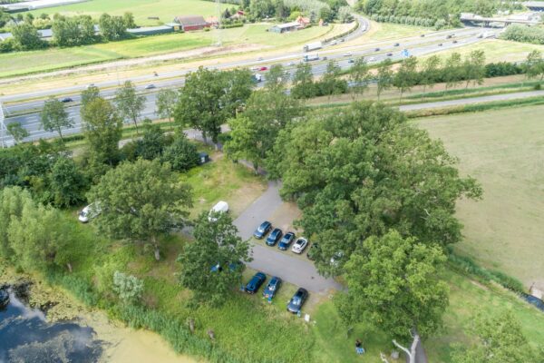 Luchtfoto van een parkeerplaats langs de Fortweg met geparkeerde auto's, omringd door bomen en nabij een snelweg.