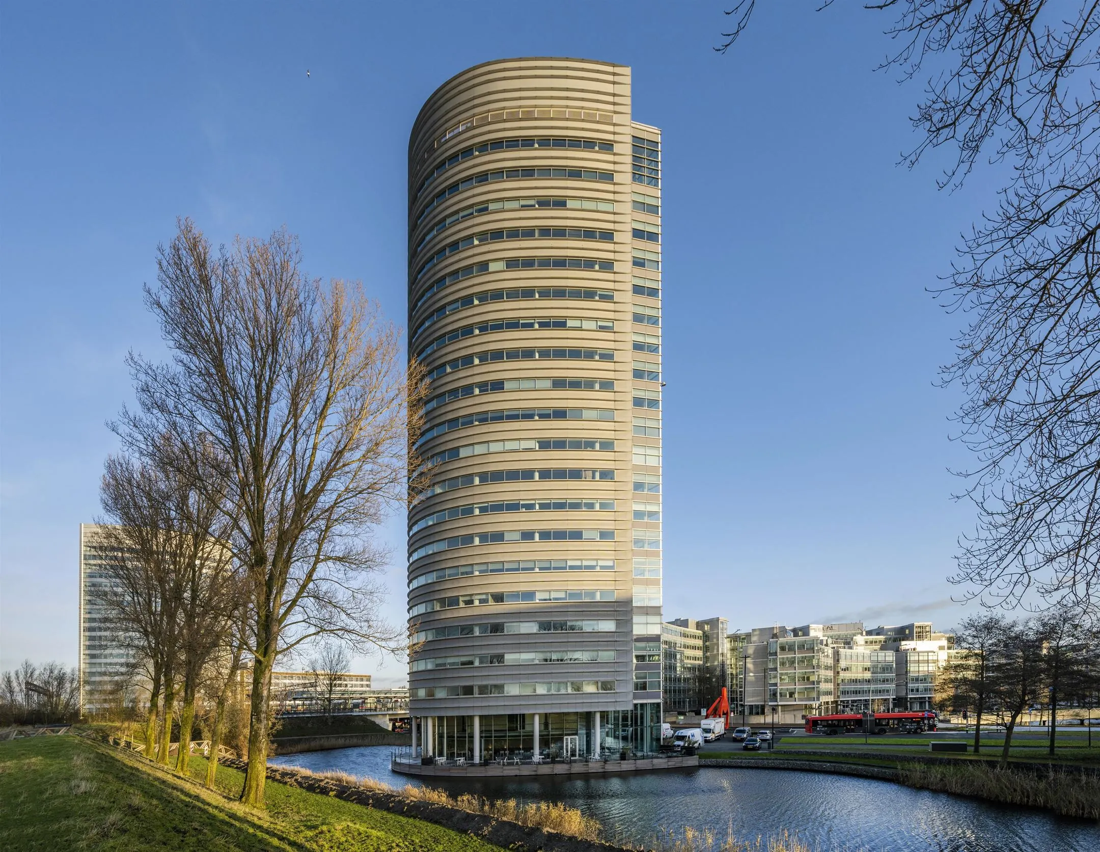 Rond kantoorgebouw 157_2160 aan het water met omliggende moderne architectuur en bomen.