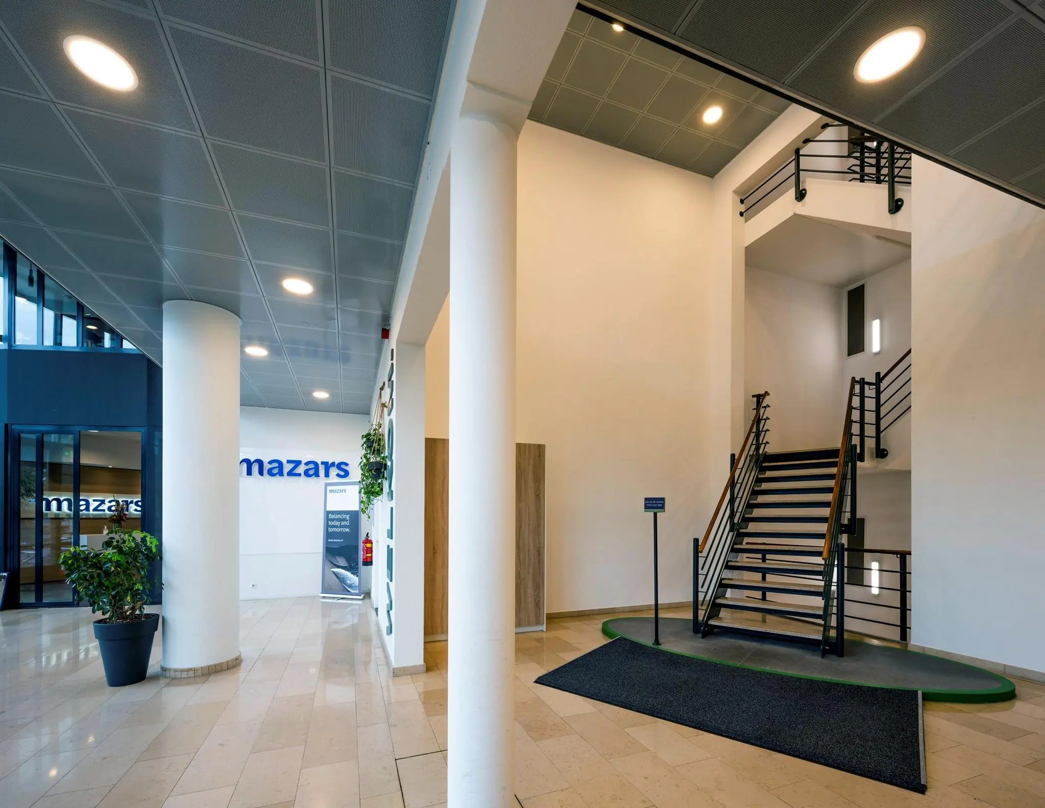 Moderne entreehal van het kantoorgebouw aan de Watermanweg met een trap, planten en het logo van Mazars op de muur.