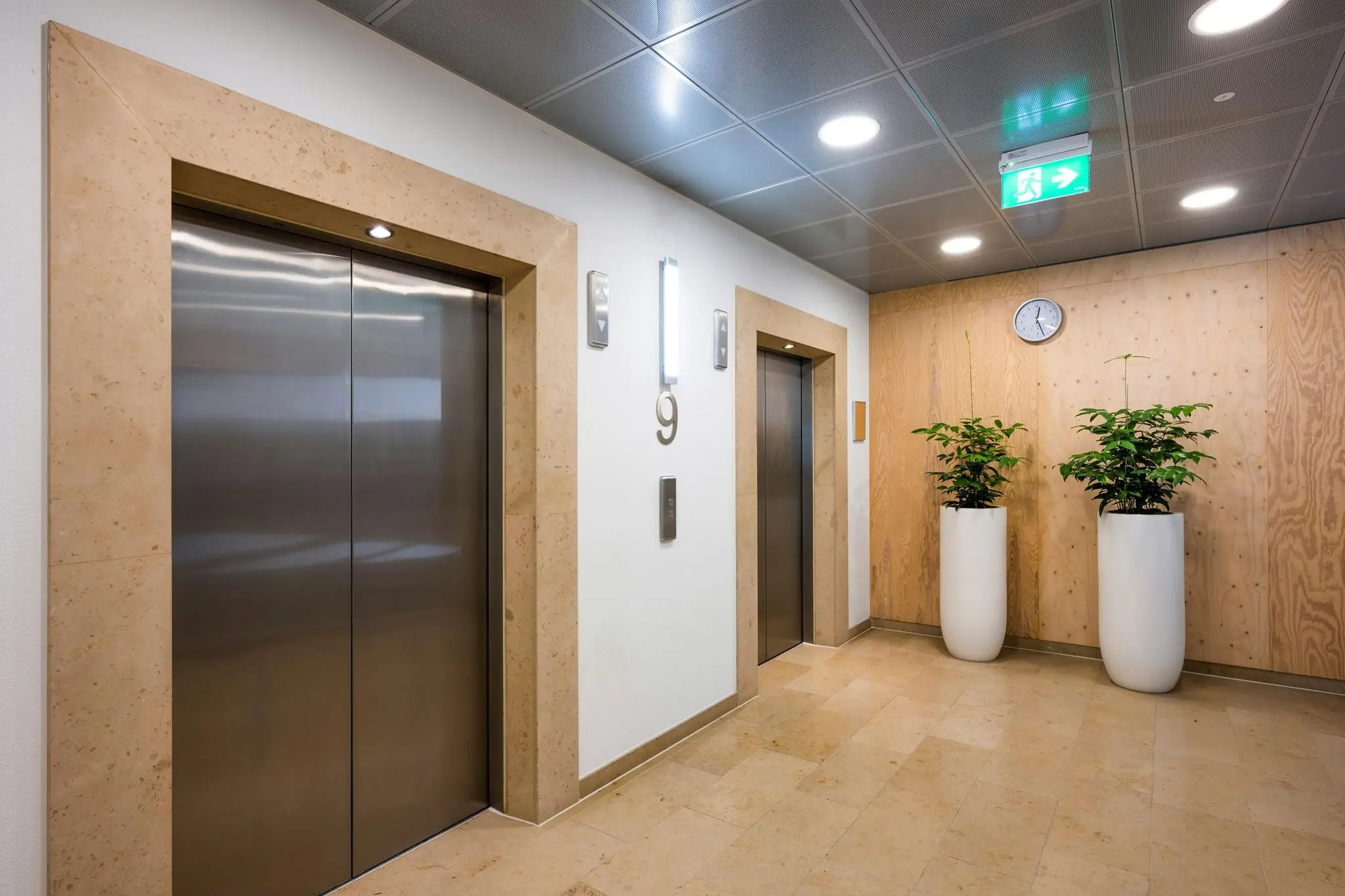 Moderne liftlobby op de negende verdieping van een kantoorgebouw aan de Watermanweg, met twee liften, planten en een klok aan de wand.