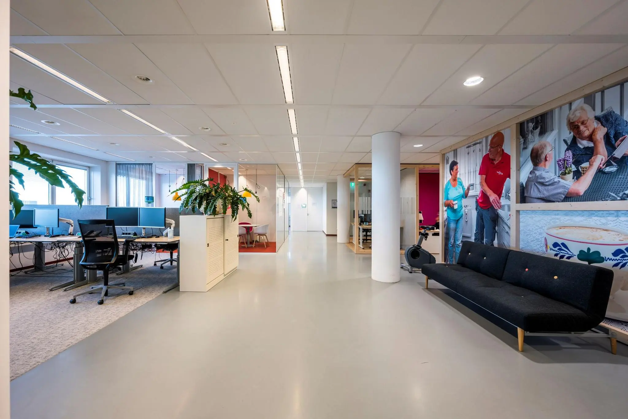 Moderne kantoorruimte aan de Watermanweg met werkplekken, vergaderruimtes en een grote wandfoto van zorgverleners.