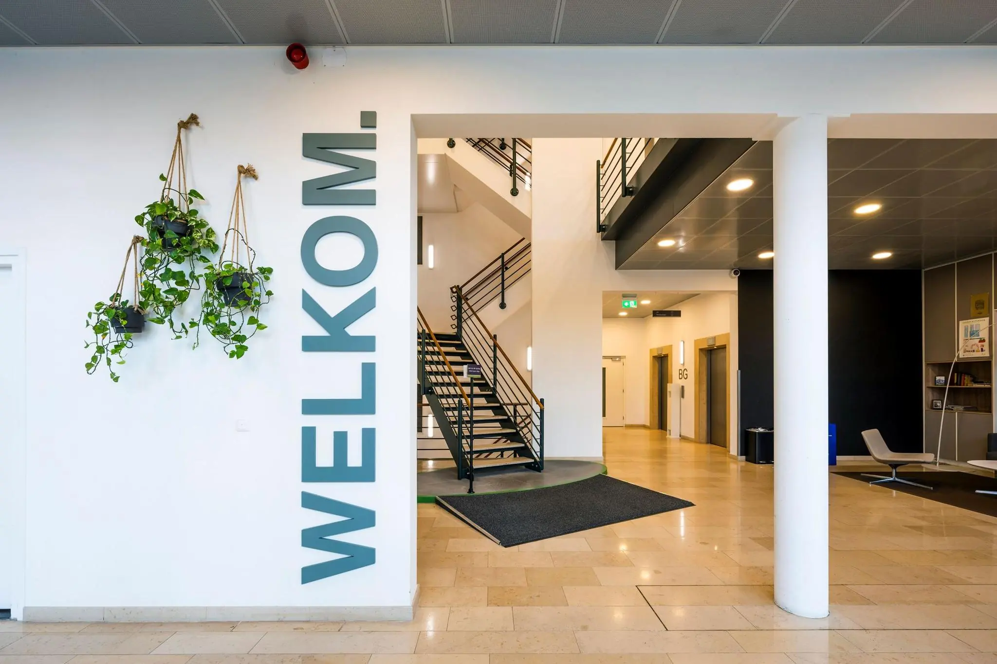 Ingang van een modern kantoorpand aan de Watermanweg met een welkom-tekst op de muur, hangplanten en een centrale trap.