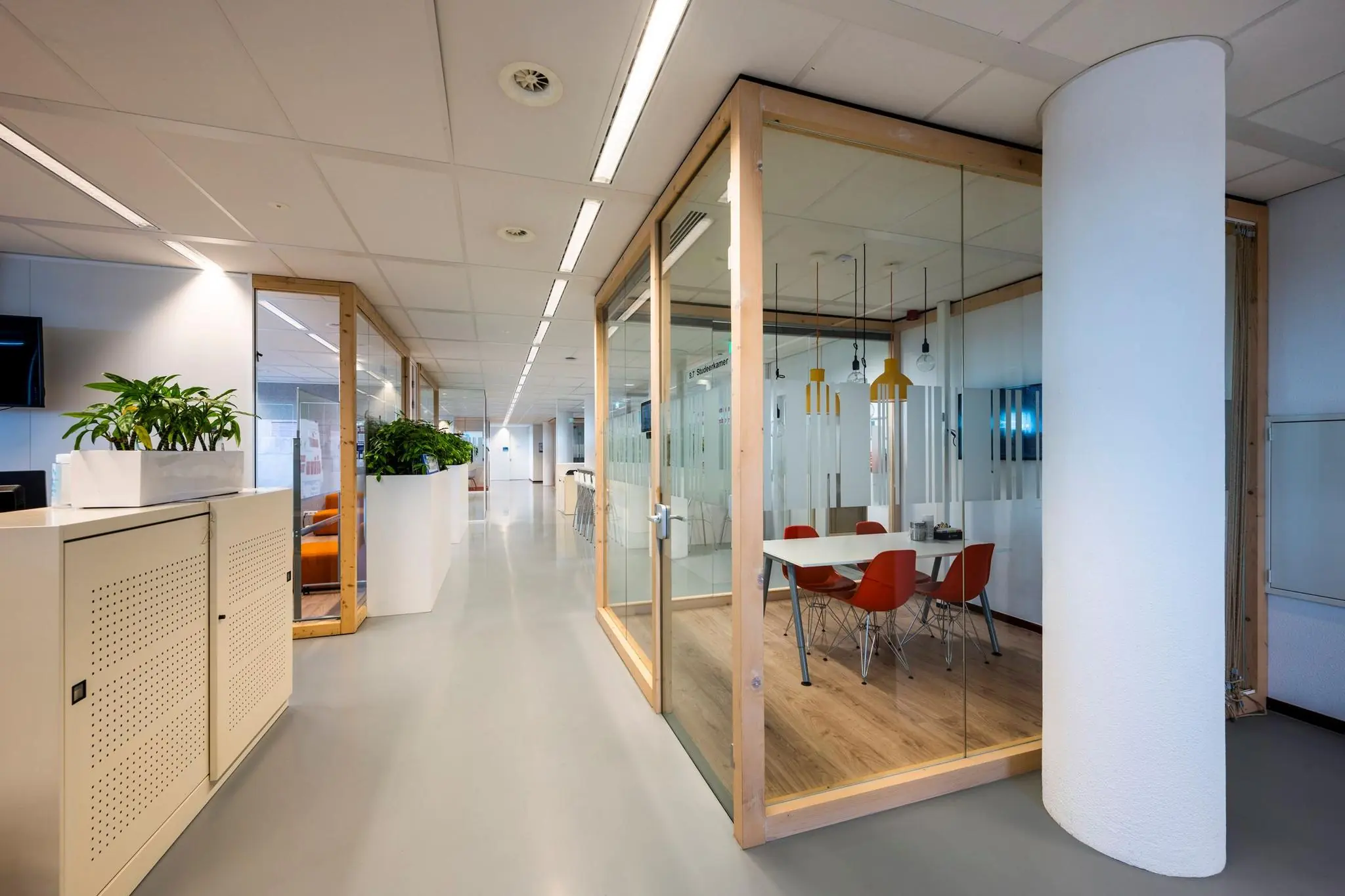 Moderne kantoorruimte aan de Watermanweg met glazen vergaderruimte, oranje stoelen en strakke inrichting.
