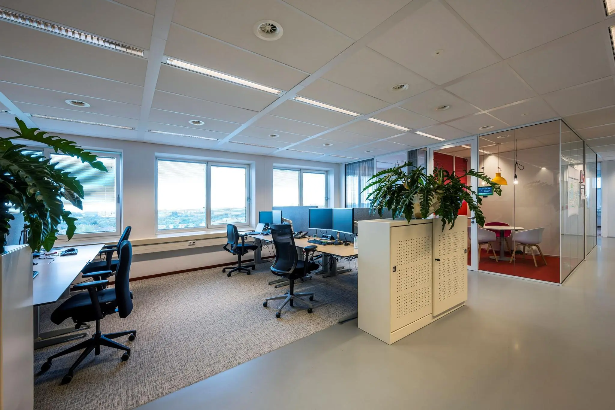 Modern kantoorinterieur aan de Watermanweg met open werkplekken, bureaustoelen, computers en een aparte vergaderruimte met glazen wanden.