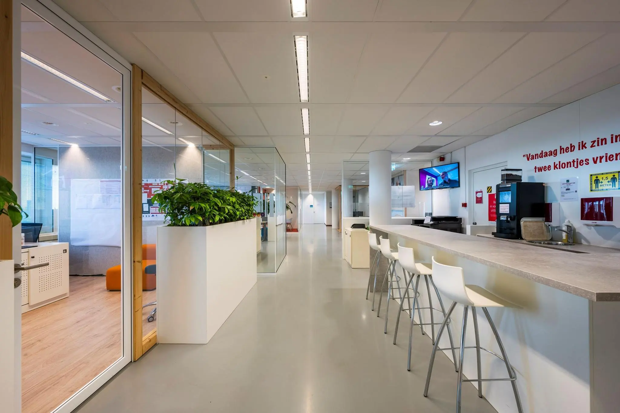 Moderne kantoorruimte aan de Watermanweg met een open gang, glazen wanden, een koffiehoek en hoge witte stoelen.