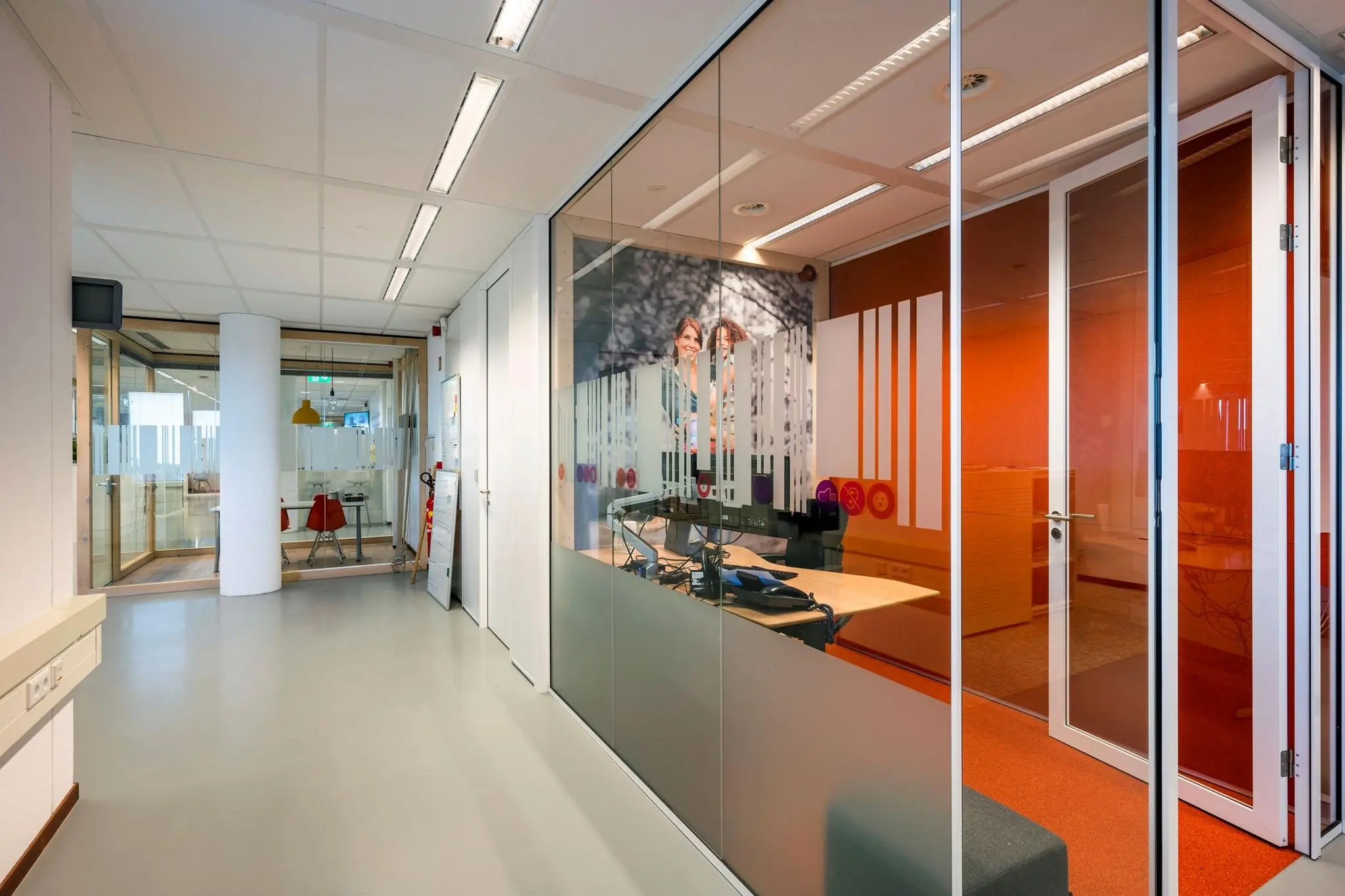 Gang in een modern kantoorpand aan de Watermanweg met glazen vergaderruimtes en kleurrijke interieurdetails.